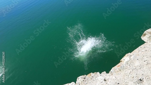 Teen boy jumping off a cliff rock into the water, extreme