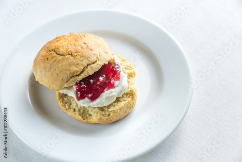 Scone with cream and cherry jam on the plate