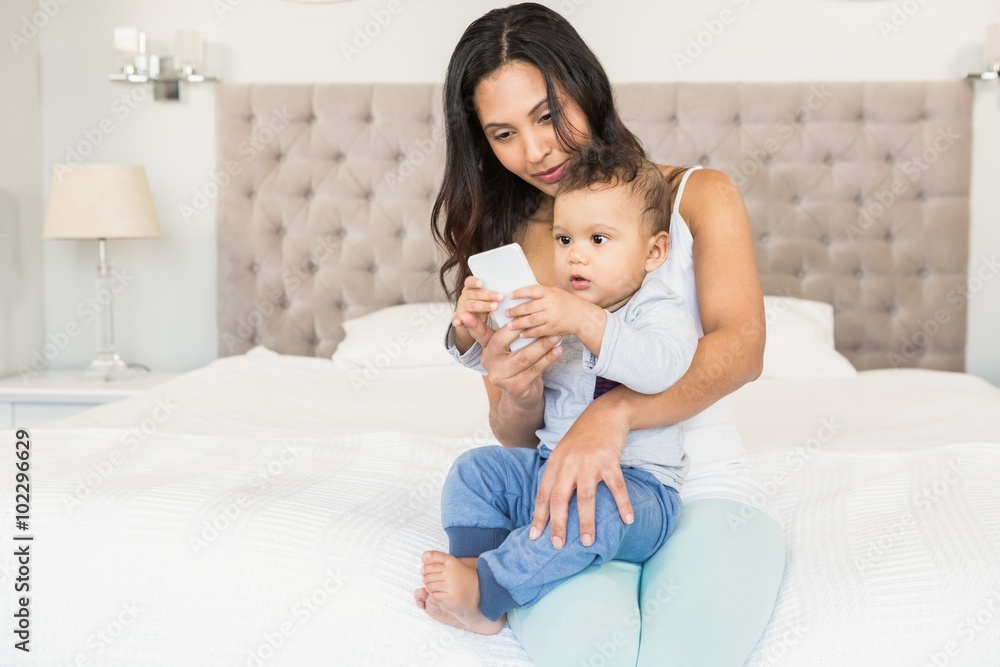 Happy brunette holding her baby and using smartphone Happy brunette holding her baby and using smartphone