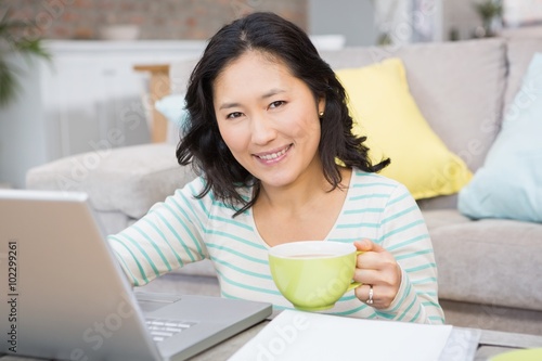 Smiling brunette using laptop and holding mug