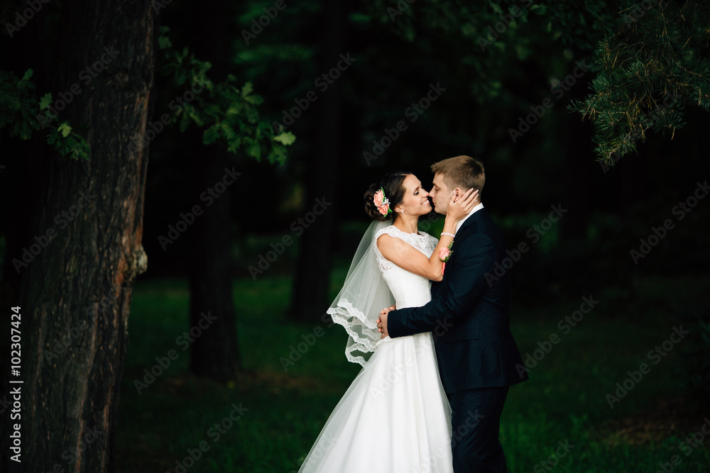 Elegant stylish groom embraces with his happy bride in park