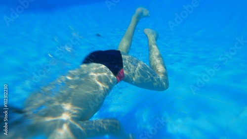 Caucasian child boy teen dives underwater in outdoor swimming pool. Sun tanning, swimming, tourism, rest and relaxation .