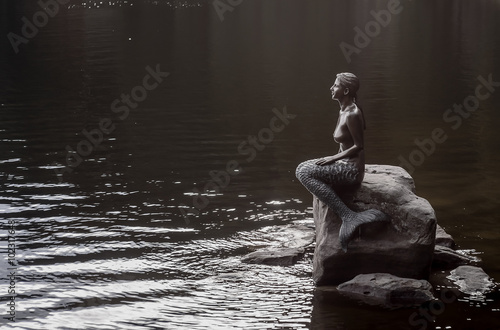 Statue of girl-mermaid on a rock near a pond