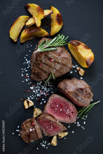 Rare beef filet mignon steak served with baked potato slices