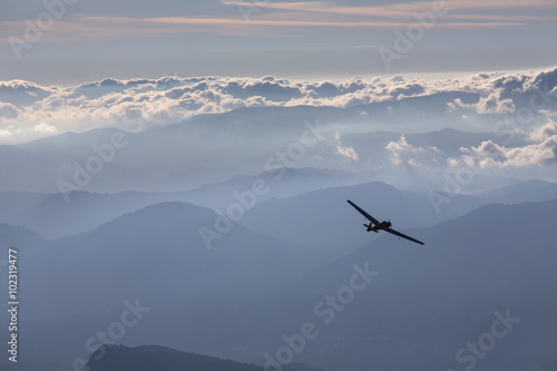 Sillhouette of small plane over clouds and mountains