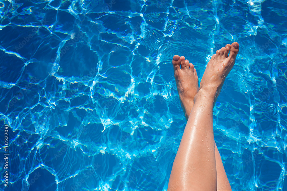 woman legs splashing in tropical swimming pool
