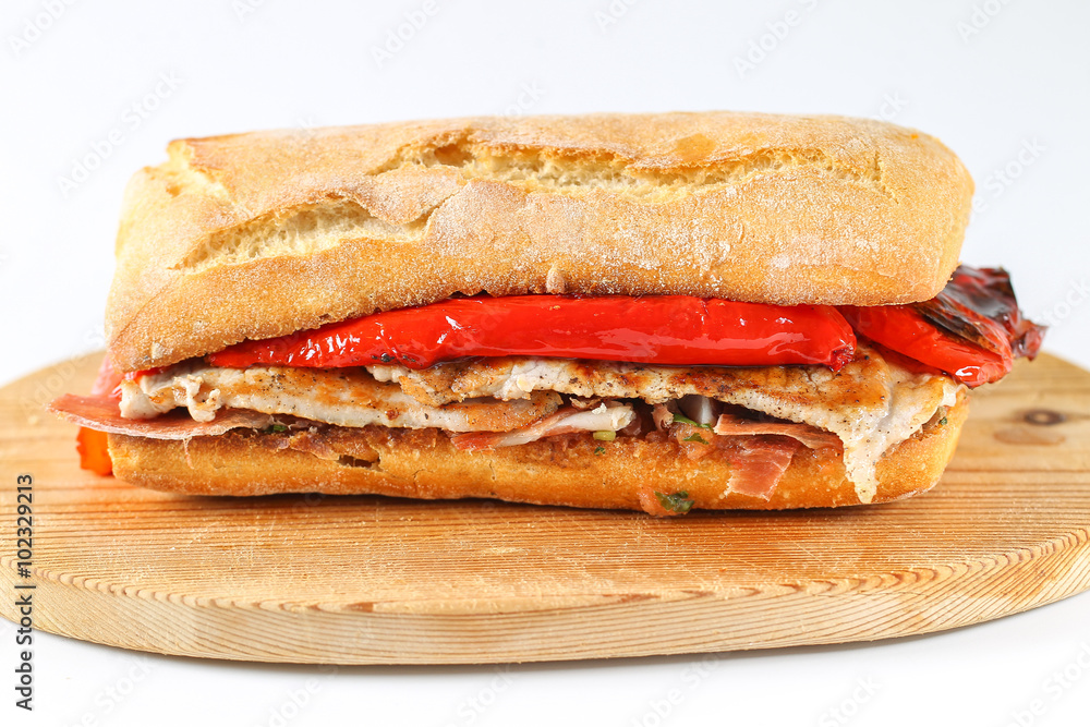 Tasty pork grilled serranito sandwich in a ciabatta with ham and red pepper on a white background Tasty pork grilled serranito sandwich in a ciabatta with ham and red pepper on a white background