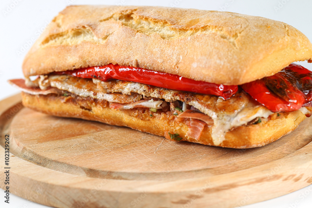 Tasty pork grilled serranito sandwich in a ciabatta with ham and red pepper on a white background Tasty pork grilled serranito sandwich in a ciabatta with ham and red pepper on a white background