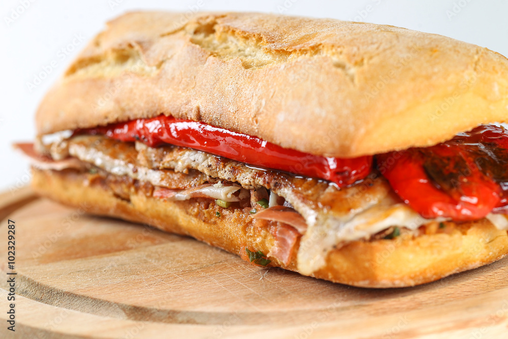 Tasty pork grilled serranito sandwich in a ciabatta with ham and red pepper on a white background Tasty pork grilled serranito sandwich in a ciabatta with ham and red pepper on a white background