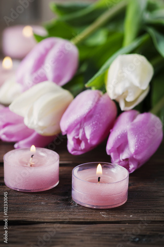 Pink and white tulips and candles on the wooden table