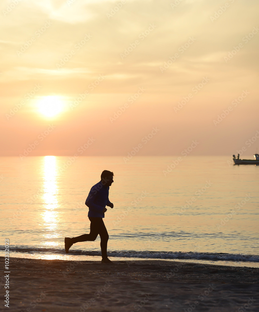 Fototapeta premium silhouette young sport man running outdoors on beach at sunset with orange sky