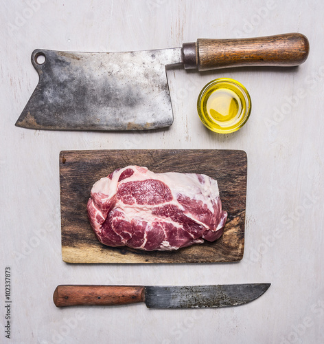 delicious raw pork steak on a cutting board with a meat cleaver and a knife for meat on wooden rustic background top view close up