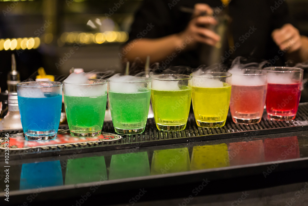 A group of shot glasses with a rainbow of colored drinks.