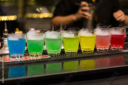 A group of shot glasses with a rainbow of colored drinks. © akedesign