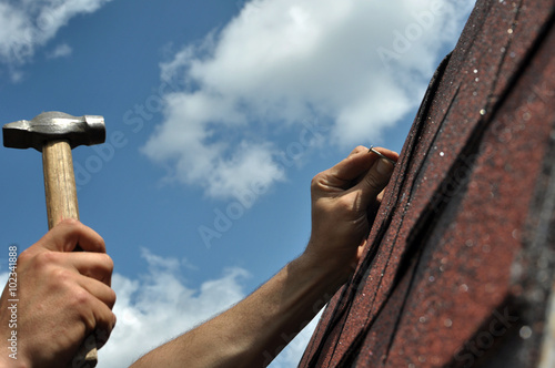 Hand with a hammer to drive a nail, roof repairs photo