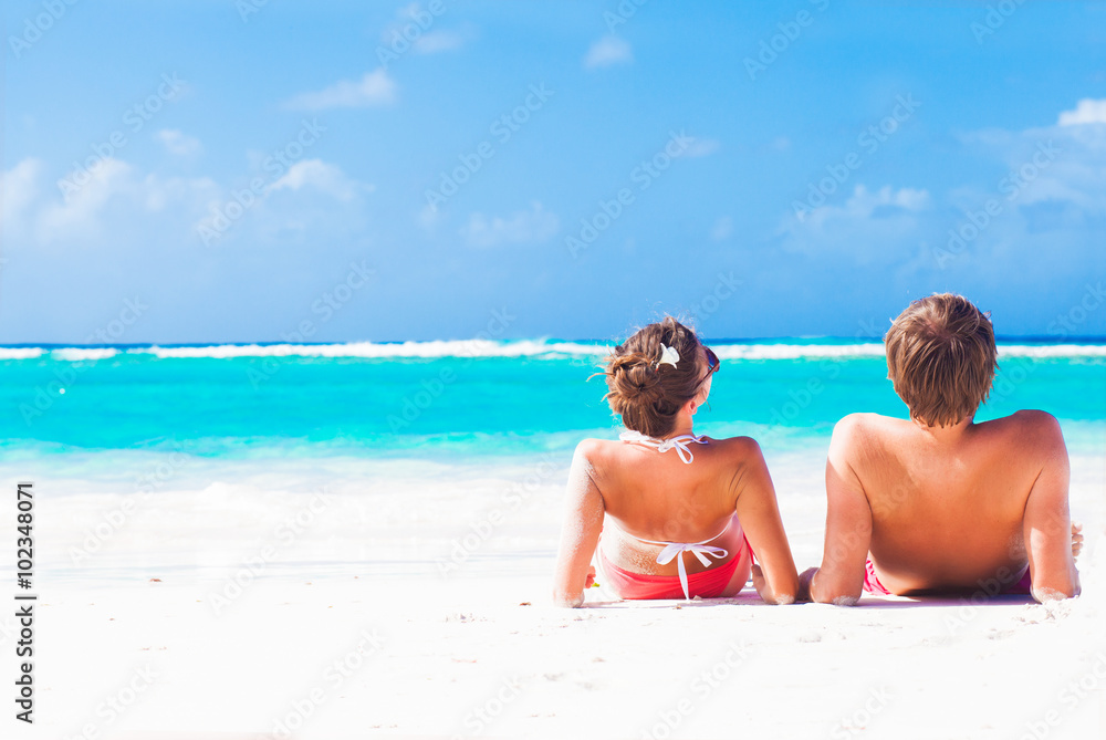 back view of happy young caucasian couple sitting at the beach back view of happy young caucasian couple sitting at the beach