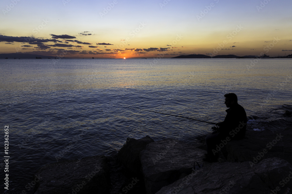 Scenic view of beautiful sunset with a fisherman silhouette sitting on the rocks near seaside