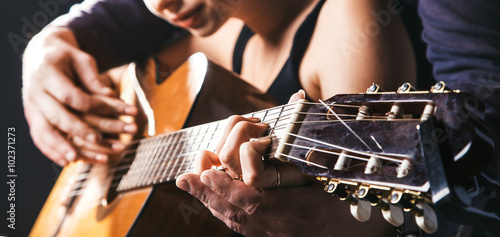 blurred man's hands playing acoustic guitar, and teaching girl to play on guitar.