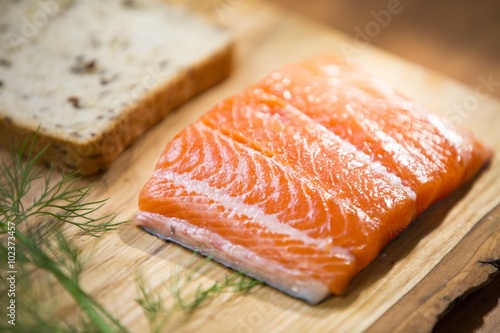 Close up of a fresh salmon steak fillet lying on a wooden plate with a dill, bread and lemon