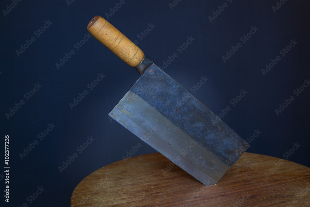 Traditional Chinese cleaver with carbon steel blade and bamboo wood handle stuck in round cutting board with dark background