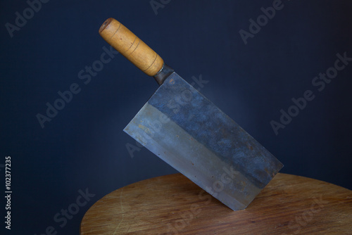 Traditional Chinese cleaver with carbon steel blade and bamboo wood handle stuck in round cutting board with dark background