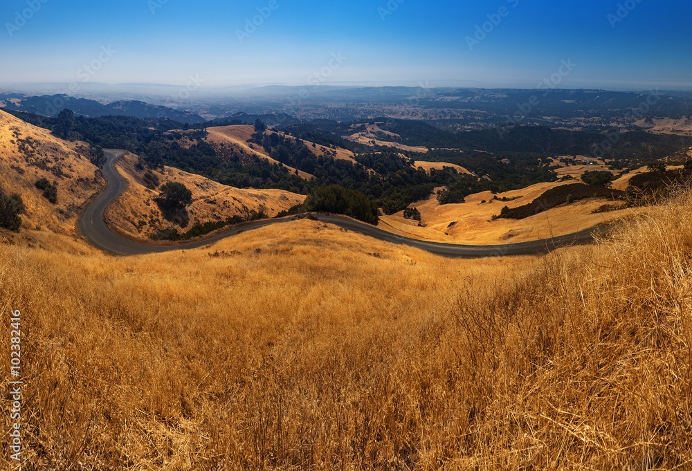 Wide angle curvy roads and yellow fields through the mountains with blue sky in summer, California, USA, America