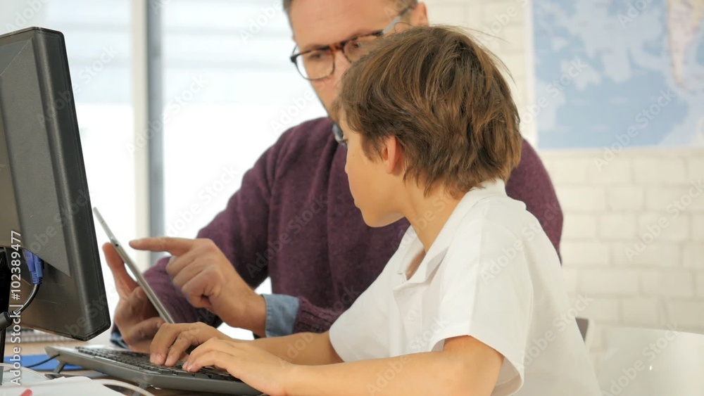 Teacher in computing class assisting kid with tablet Teacher in computing class assisting kid with tablet