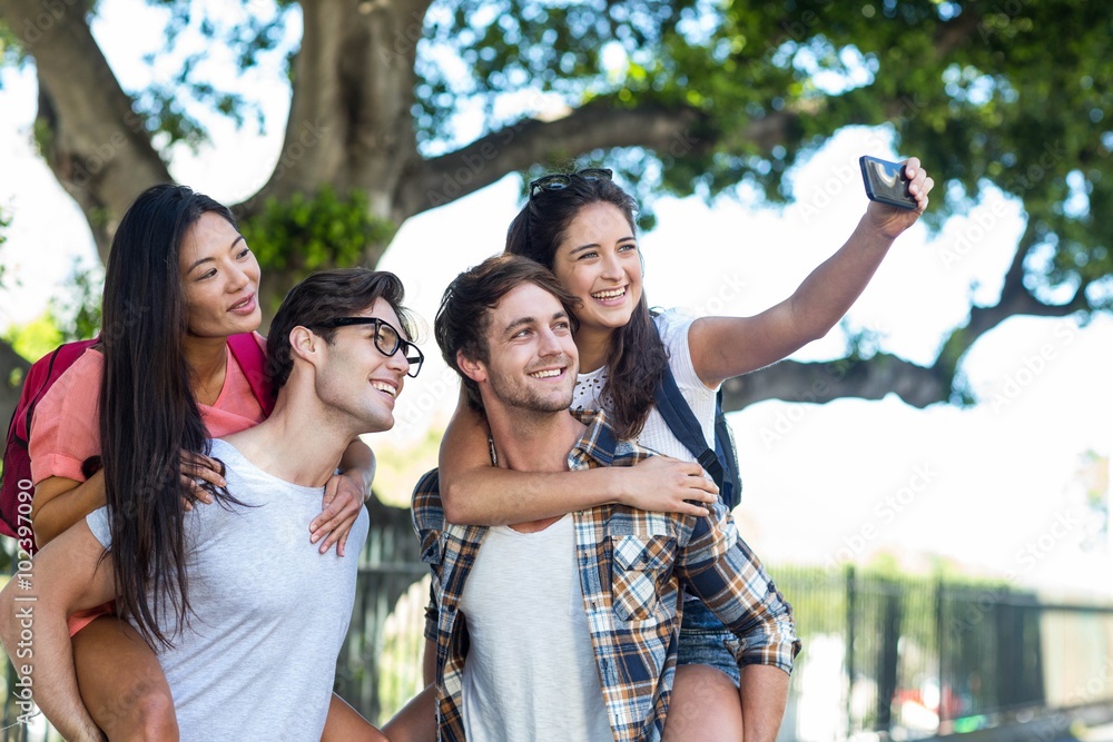 Hip men giving piggy back to their girlfriends and taking selfie