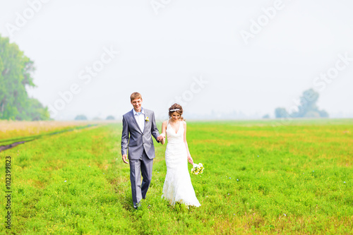 A young couple in love bride and groom, wedding day in summer. Enjoy a moment of happiness and love in a field. Bride in a luxurious wedding dress on a background bright blue sky with clouds.