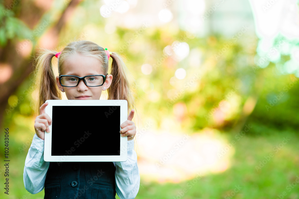 Adorable little girl holding tablet PC outdoors in autumn sunny day Adorable little girl holding tablet PC outdoors in autumn sunny day