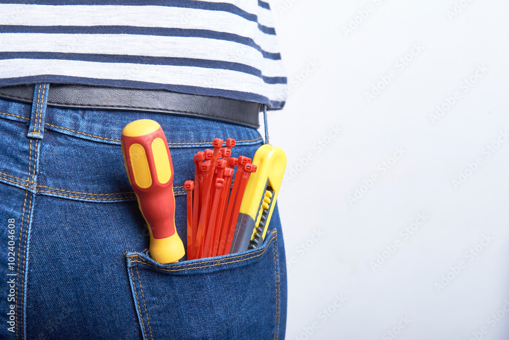 Tools for electrician in back pocket of blue jeans worn by a woman