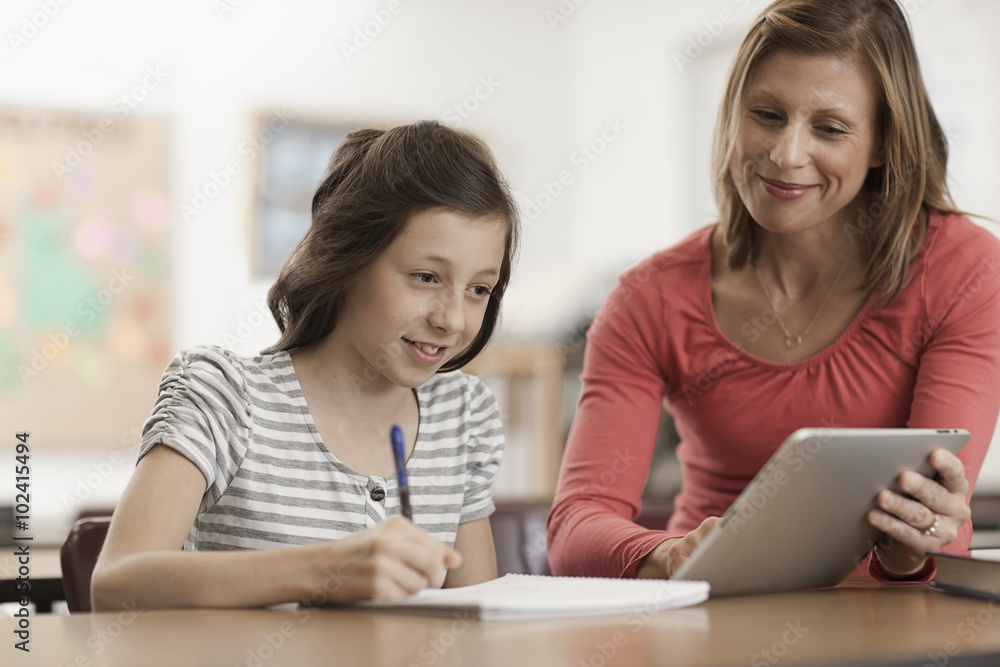 An adult woman teacher and a girl looking at a digital tablet. An adult woman teacher and a girl looking at a digital tablet.