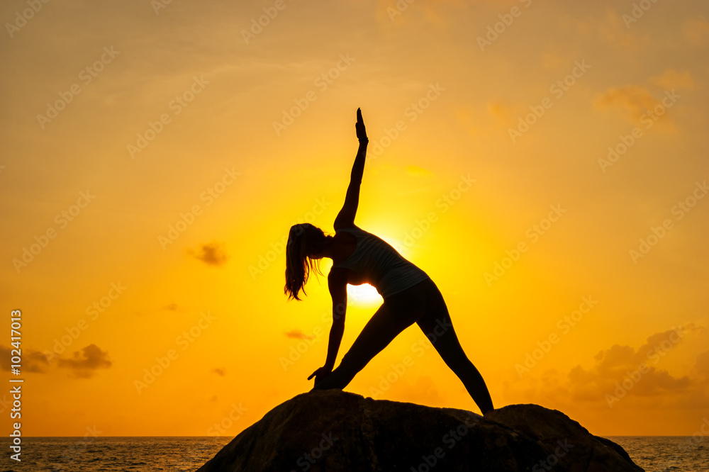 Woman practices yoga on the rocks against the sea
