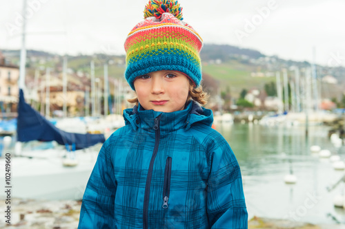 Outdoor close up portrait of a cute little boy of 4-5 years old, wearing colorful hat and waterproof blue coat
