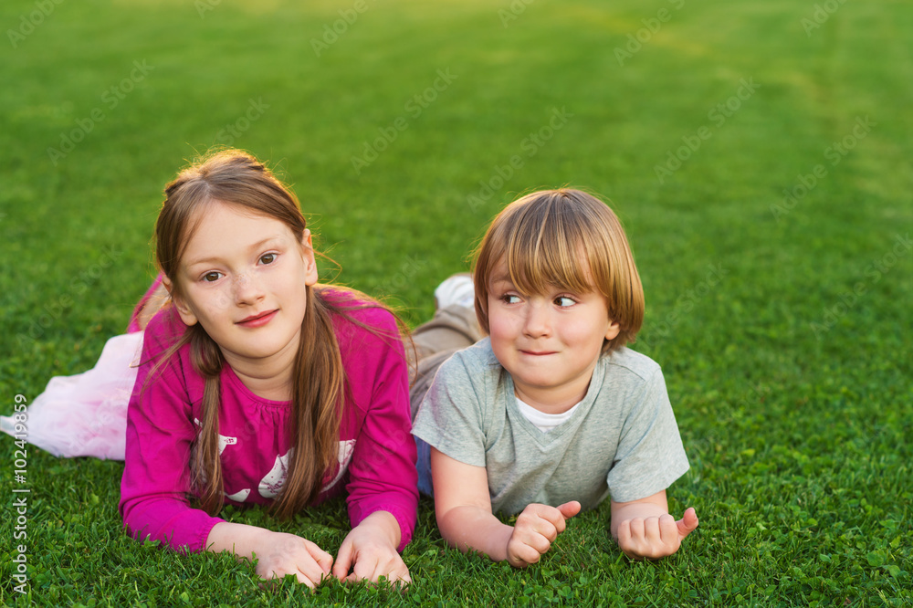 Outdoor portrait of two cute kids, laying on a bright green lawn Outdoor portrait of two cute kids, laying on a bright green lawn