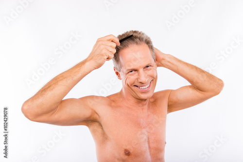 Handsome positive shaved aged man combing his hair