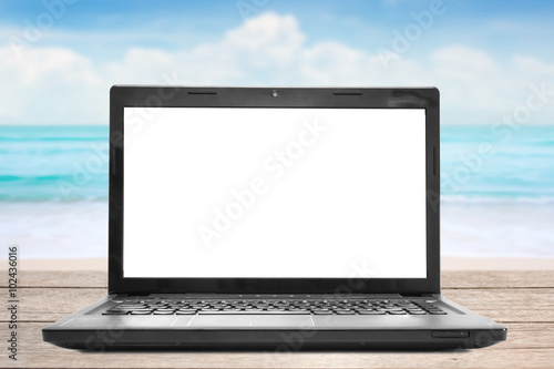 Laptop with blank screen on wooden table blurred sea and beach background © ampcool