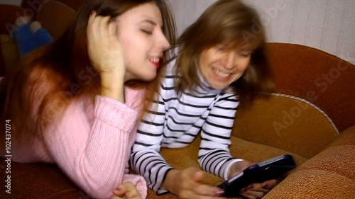 Mother and daughter lying on the couch looking at the tablet, talking and laughing