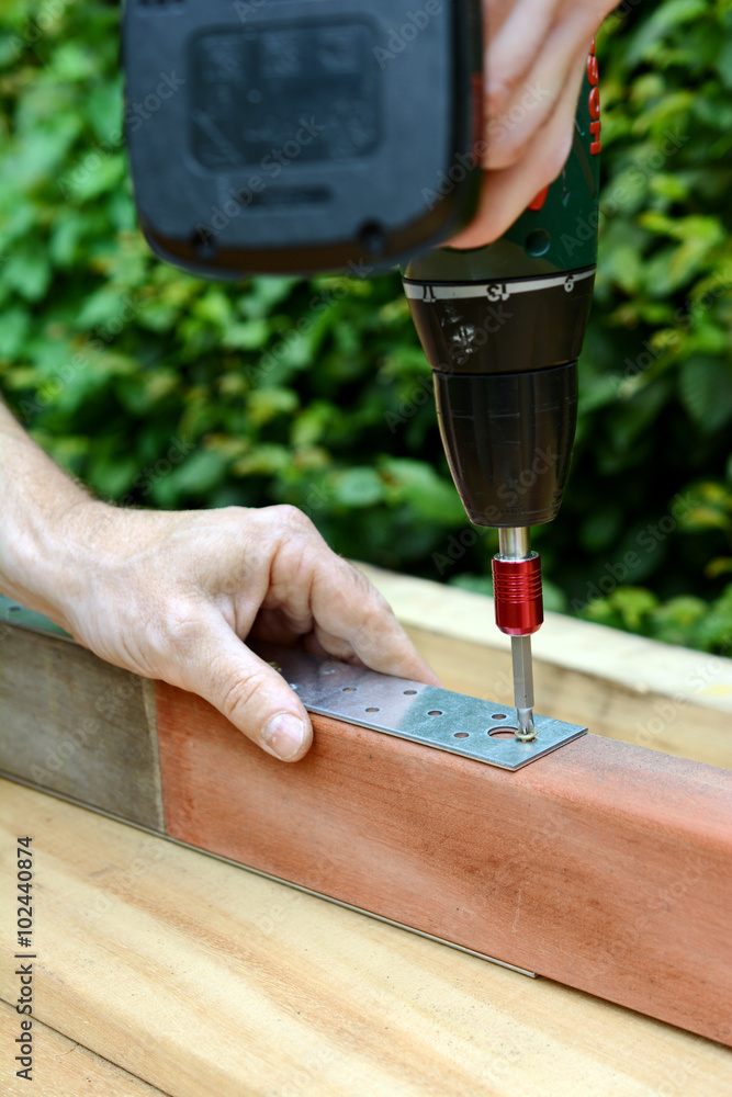 Schreiner oder Handwerker in Garten dreht Schraube mit Akkuschrauber in Holzbalken für Terrasse Schreiner oder Handwerker in Garten dreht Schraube mit Akkuschrauber in Holzbalken für Terrasse