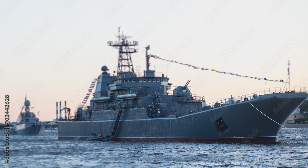 Grey modern battleship warship sailing in still water against summer sky with one more warship in the background Grey modern battleship warship sailing in still water against summer sky with one more warship in the background