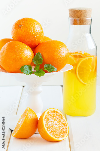 Ripe oranges and a bottle of fresh juice. White wooden background