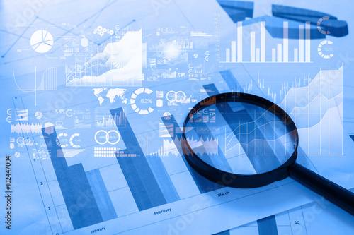 Magnifying glass and documents with analytics data lying on tabl