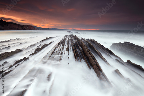 Waves over the rocks at sunset in Itzurun beach photo
