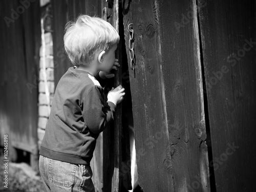Children's curiosity - boy looking throw shed's door photo