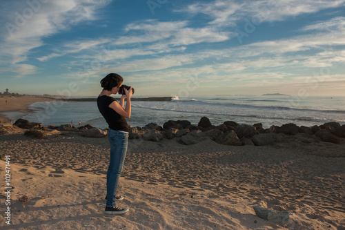 Female teen photographer pointer her camera at the beach. 