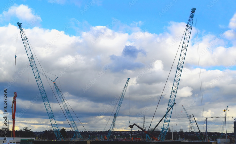 Construction site with tall industrial cranes and clouds in background