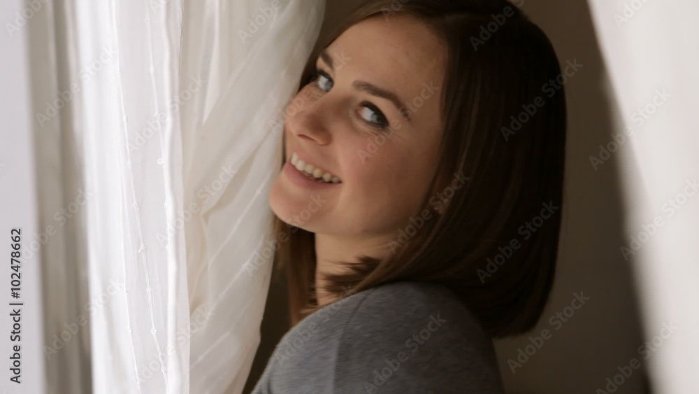 Smiling woman looking at camera and hiding behind the curtains Smiling woman looking at camera and hiding behind the curtains