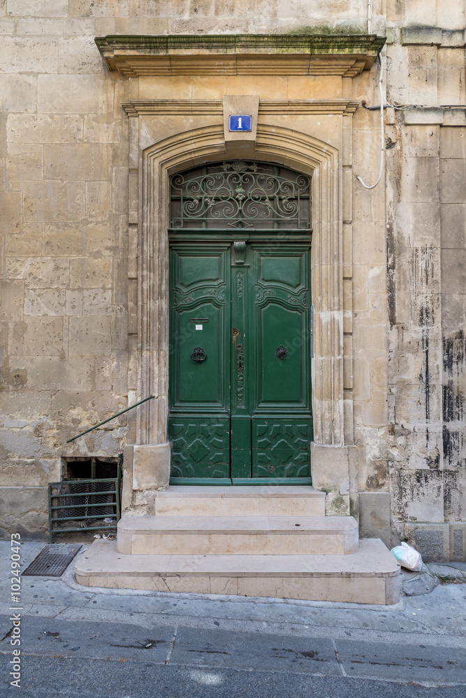 Od gate with ornaments and closed green doors in an old building in a street in Arles, France on a sunny day in the summer