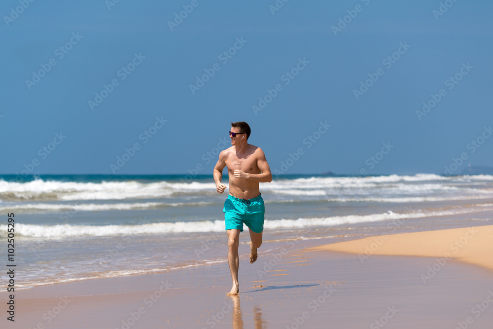 Young Man In Fitness Clothing Running Along Beach Young Man In Fitness Clothing Running Along Beach