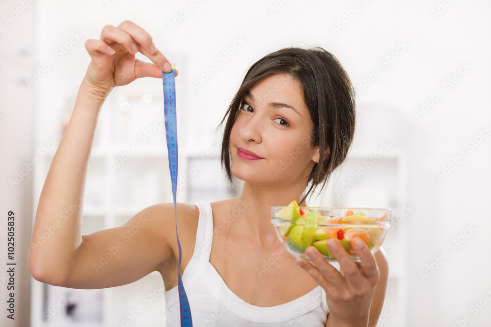 Girl holding a measuirng tape and a bowl of fruit salad. Weight loss Girl holding a measuirng tape and a bowl of fruit salad. Weight loss